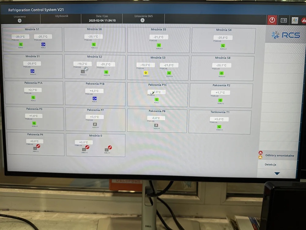 Na zdjęciu przedstawiono ekran systemu Refrigeration Control System (RCS), który umożliwia monitorowanie temperatur w poszczególnych strefach instalacji chłodniczej. Interfejs prezentuje aktualne wartości temperatur w mroźniach, pakowniach oraz innych pomieszczeniach objętych nadzorem, a także status urządzeń i sygnały alarmowe.